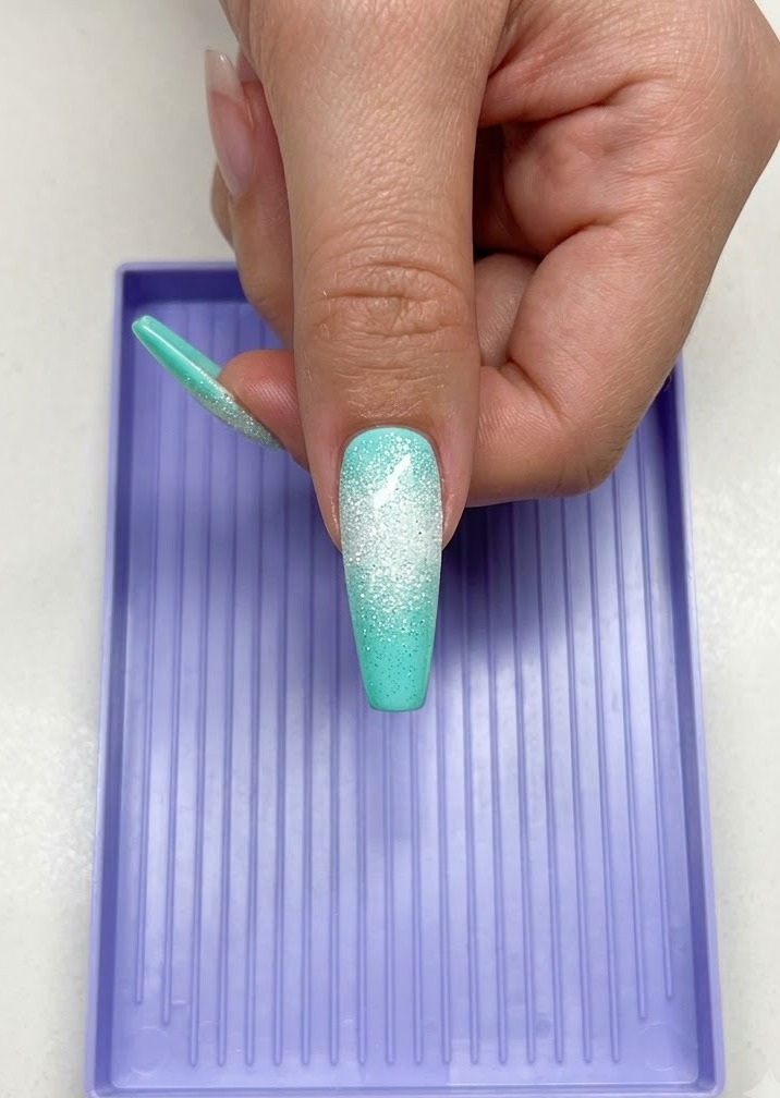 Una mano con una lunga unghia color menta e un design a stella zuccherata bianca sotto una lampada polimerizzante UV/LED viola.