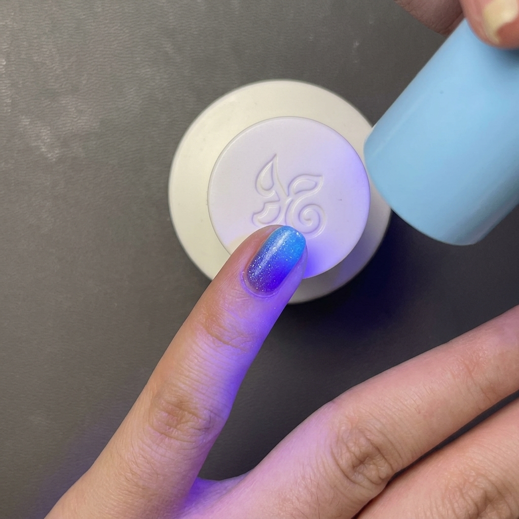 Un dito con smalto gel azzurro polimerizzato sotto una piccola lampada UV/LED portatile.