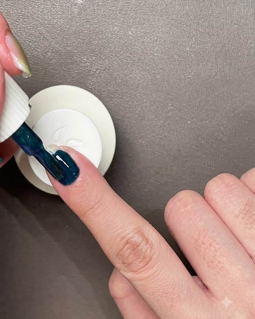 Applicazione di uno strato di smalto gel blu-verde scuro su ununghia naturale.