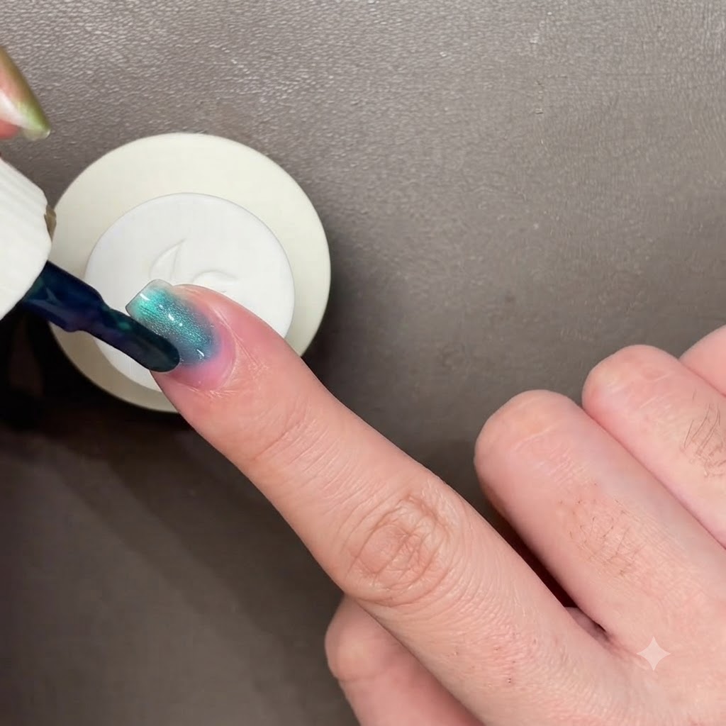 Una bacchetta magnetica nera sospesa su ununghia laccata di blu-verde scuro per manipolare lo smalto cat-eye.