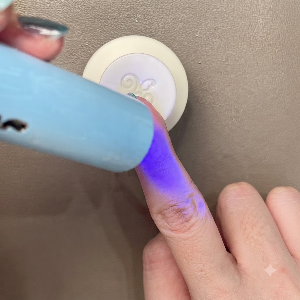 Polimerizzazione di ununghia cat-eye blu-verde sotto una piccola luce UV/LED.