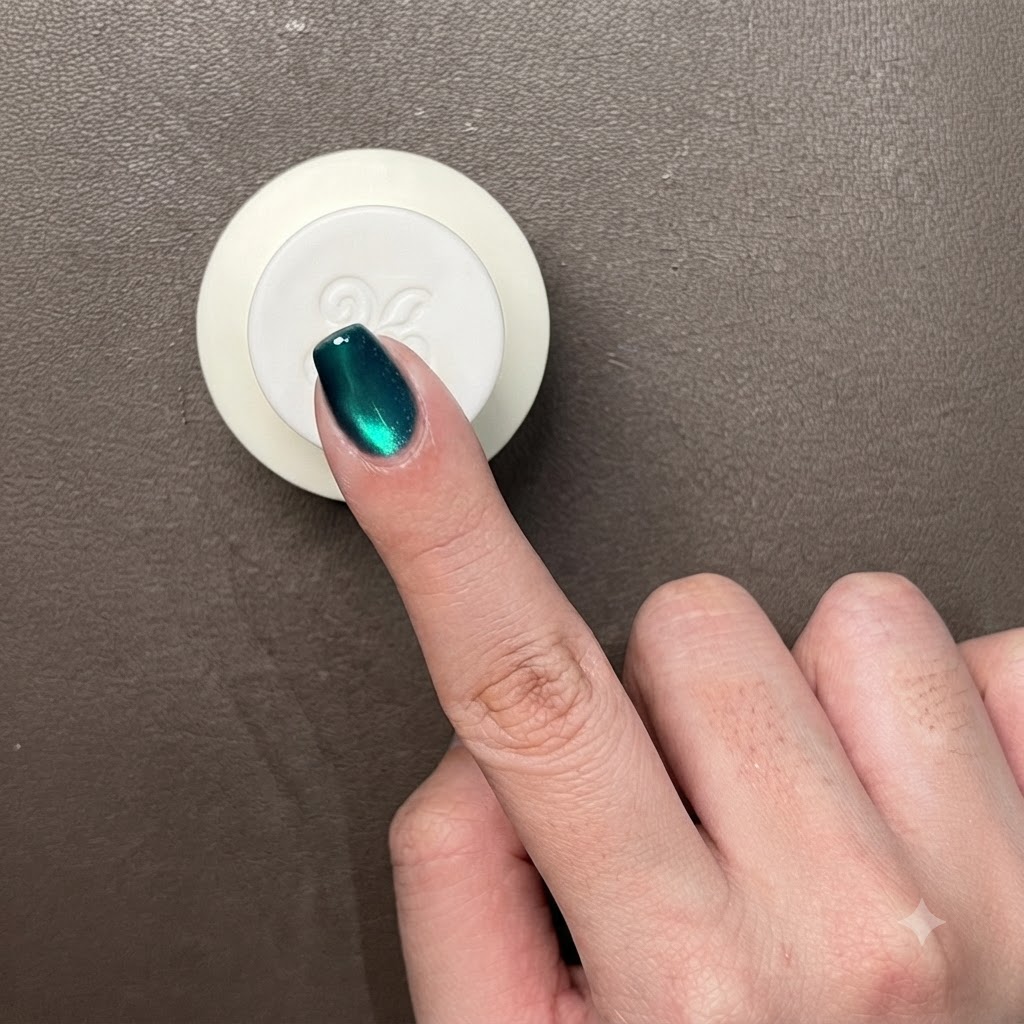 Primo piano di un dito con gel cat-eye verde metallico scuro, che mostra un riflesso luminoso circolare.