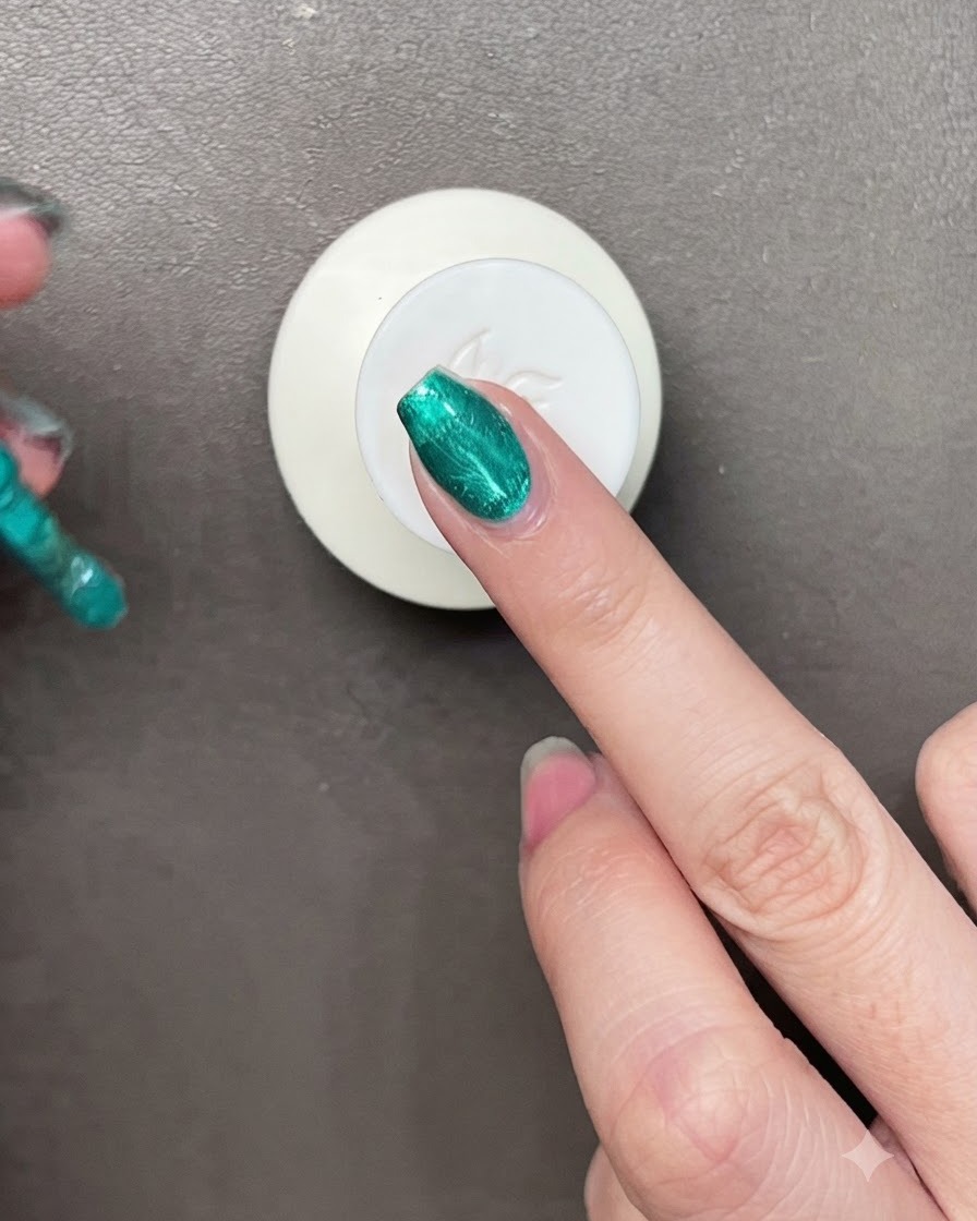 Un pennello che stende un brillante gel verde metallizzato su ununghia, con un magnetino visibile nelle vicinanze.