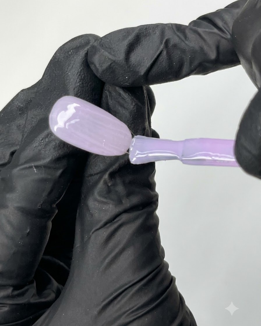 Un pennello piatto che fa scorrere uniformemente lo smalto gel viola trasparente N04 sulla superficie di una tip per unghie ovale di prova.