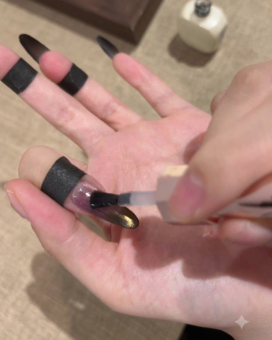 Un pennello applica un top coat sigillante lucido su ununghia sfumata nera e oro con effetto cat-eye.