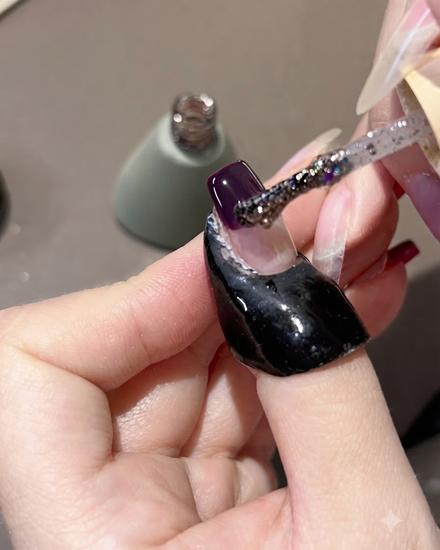 Un pennello applica il gel glitter viola sopra la punta viola scuro dellunghia, tirandolo leggermente verso lalto.