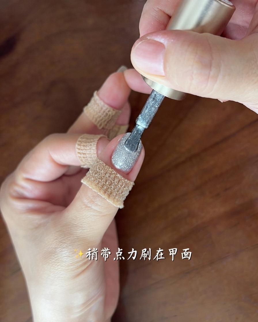 Un pennello che applica un sottile strato brillante di gel cat-eye grigio-argento su ununghia.