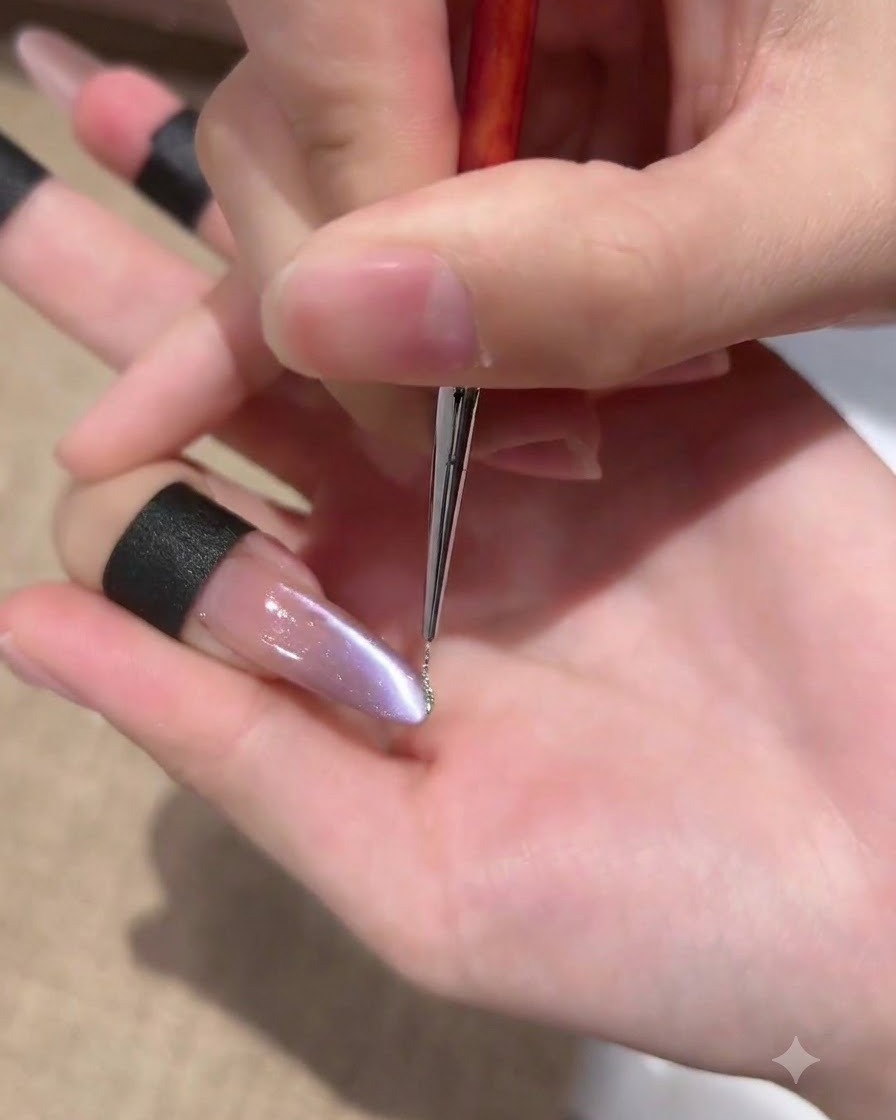 Un pennello liner sottile applica una linea molto sottile di gel glitterato argentato lungo il bordo laterale di ununghia cat-eye viola.