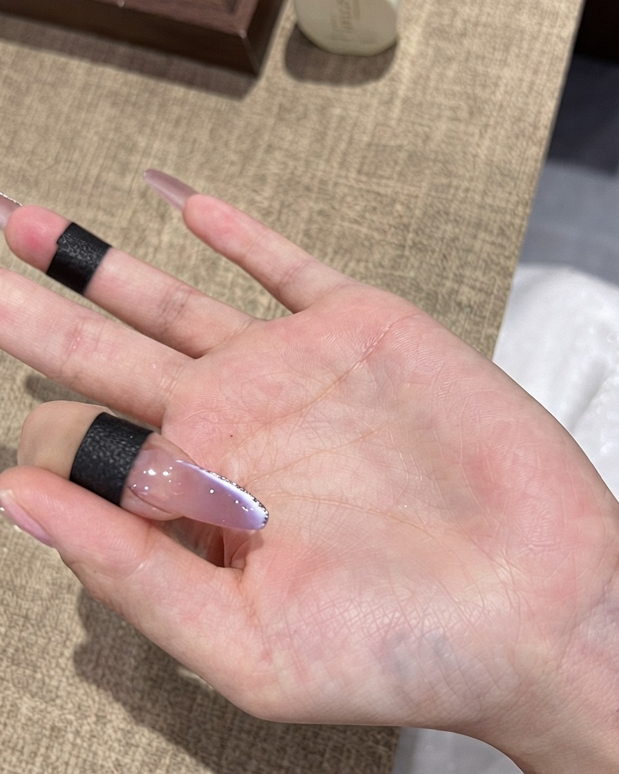 Un pennello applica un top coat lucido finale su ununghia cat-eye viola sfumata con un bordo sottile in glitter argento.