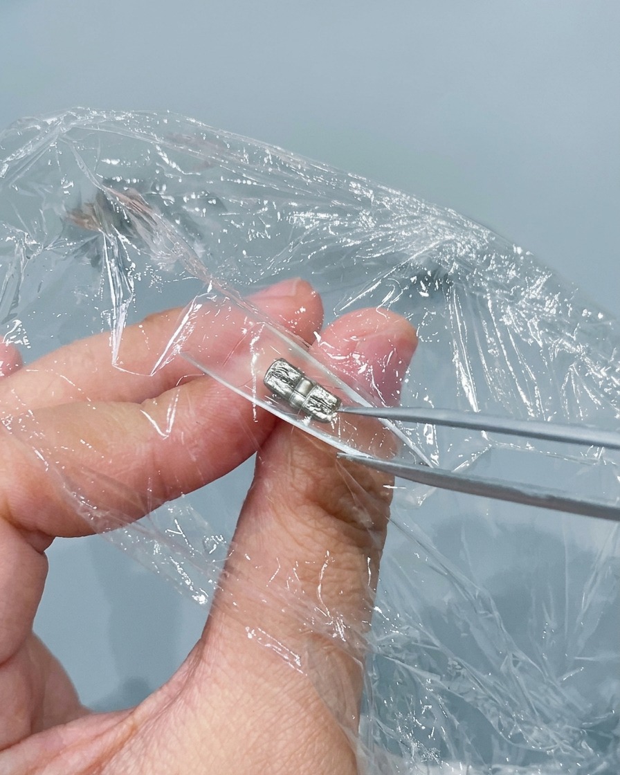 Un paio di pinzette di metallo che pizzicano e stropicciano la pellicola trasparente pressata allinterno di una tip per unghie trasparente.