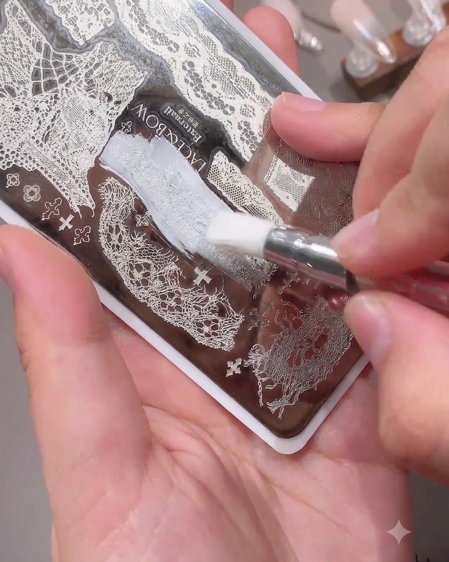 Un pennello applica dello smalto bianco su un delicato motivo in pizzo su una piastra per stamping per unghie in metallo.