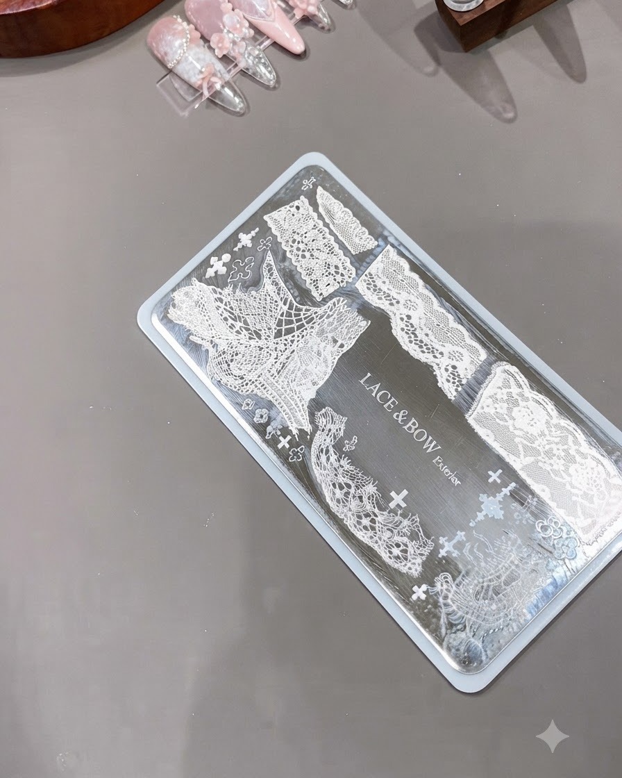 Un timbro per unghie in silicone trasparente posizionato accanto a una piastra di metallo incisa che mostra intricati motivi di pizzo bianco.