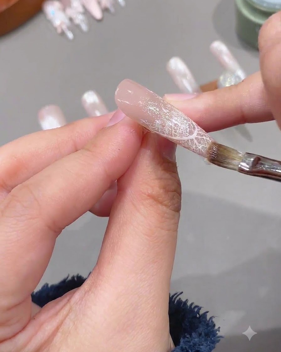 Un pennello applica uno strato trasparente di gel di rinforzo morbido su ununghia preparata con un design in pizzo.