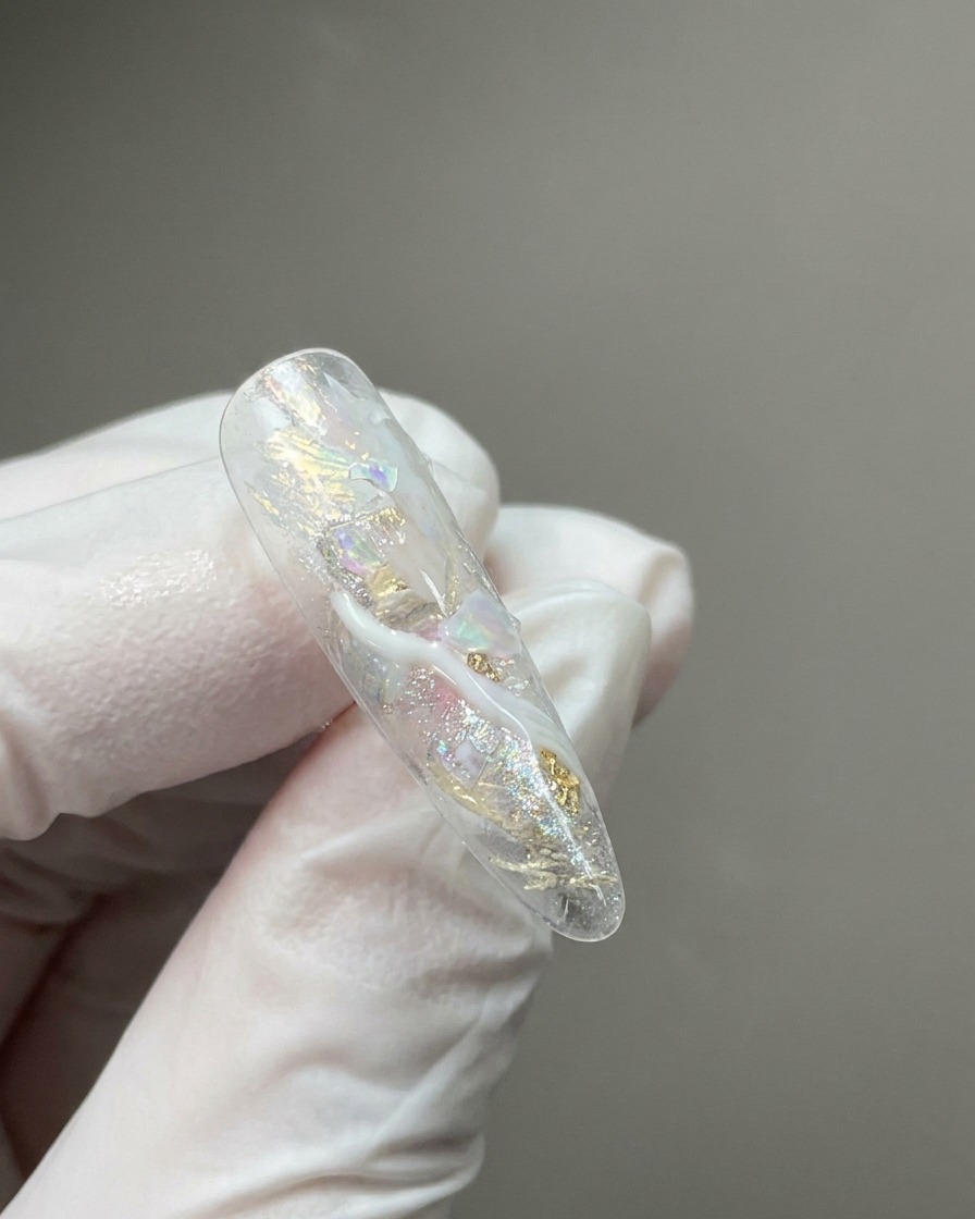Un primo piano di una tip trasparente con fiocchi iridescenti incorporati e sfumature di dettaglio effetto marmo bianco latte.