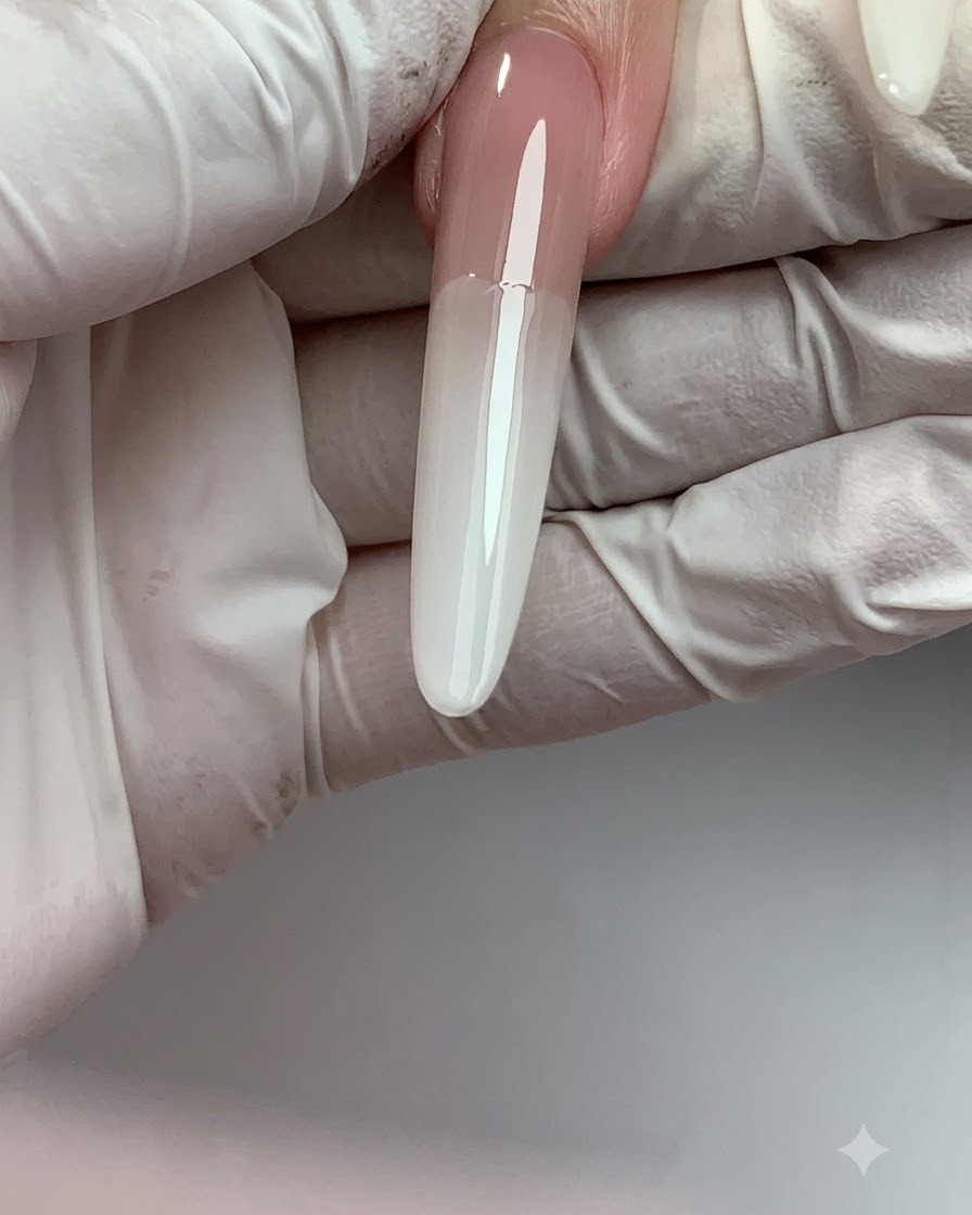 Ununghia lunga con estensione che mostra una transizione fluida a sfumatura ombré da nude in alto a bianco latte sulla punta.