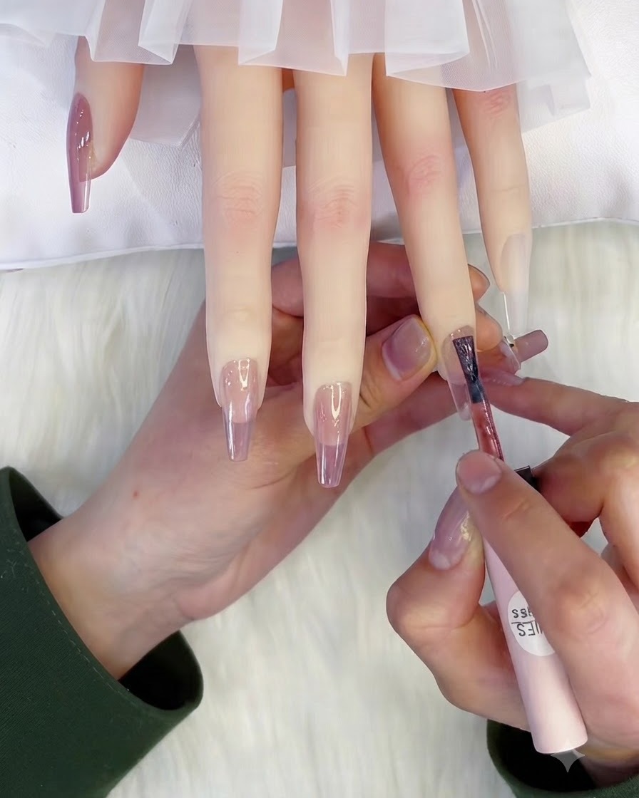 Un pennello applica una seconda mano di gel semipermanente rosa traslucido su ununghia.