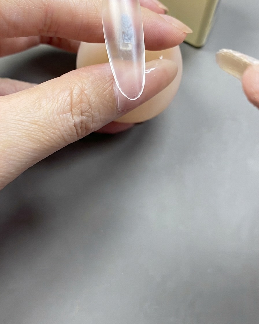 Un pennello applica uno strato trasparente di gel base su unestensione unghia trasparente.