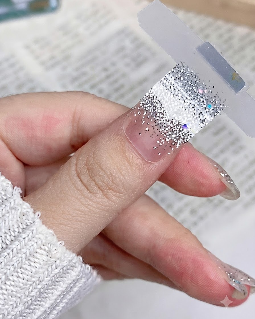 Primo piano di uno sticker per unghie con glitter argento posizionato piatto e liscio su ununghia naturale del pollice.