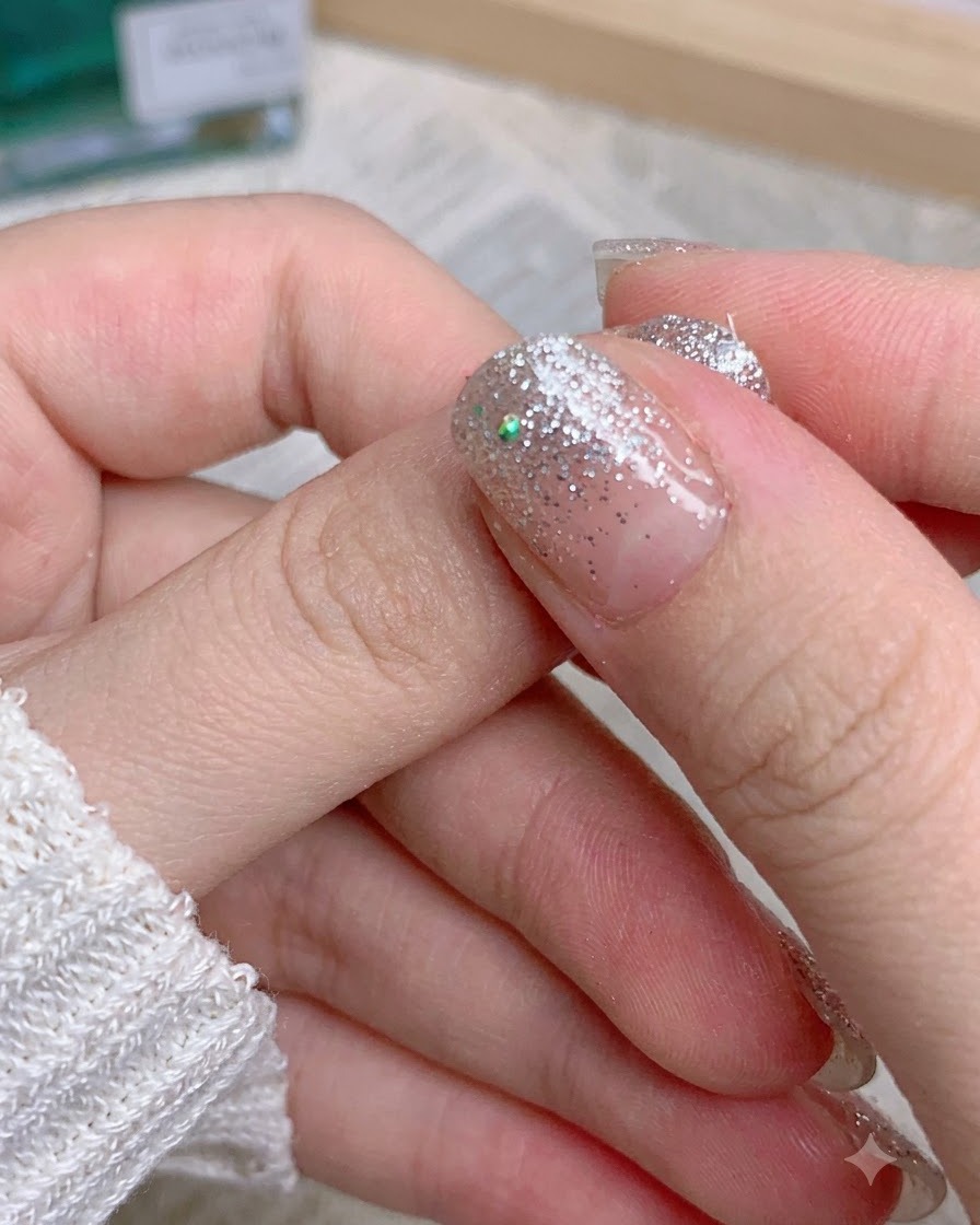 Dita che rimuovono il bordo avanzato dello sticker glitterato da un pollice con manicure.