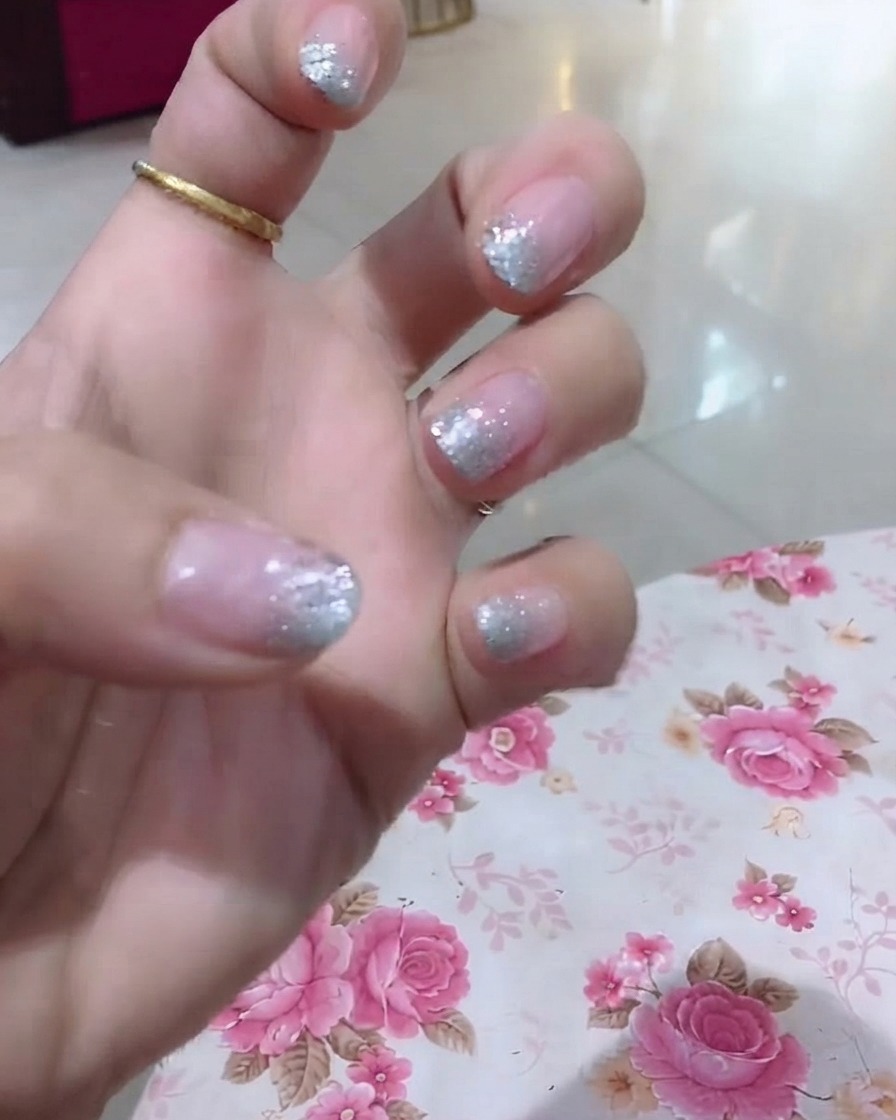 Vista ravvicinata di una mano che evidenzia lanulare con glitter e dettagli decorativi con parole sottili.