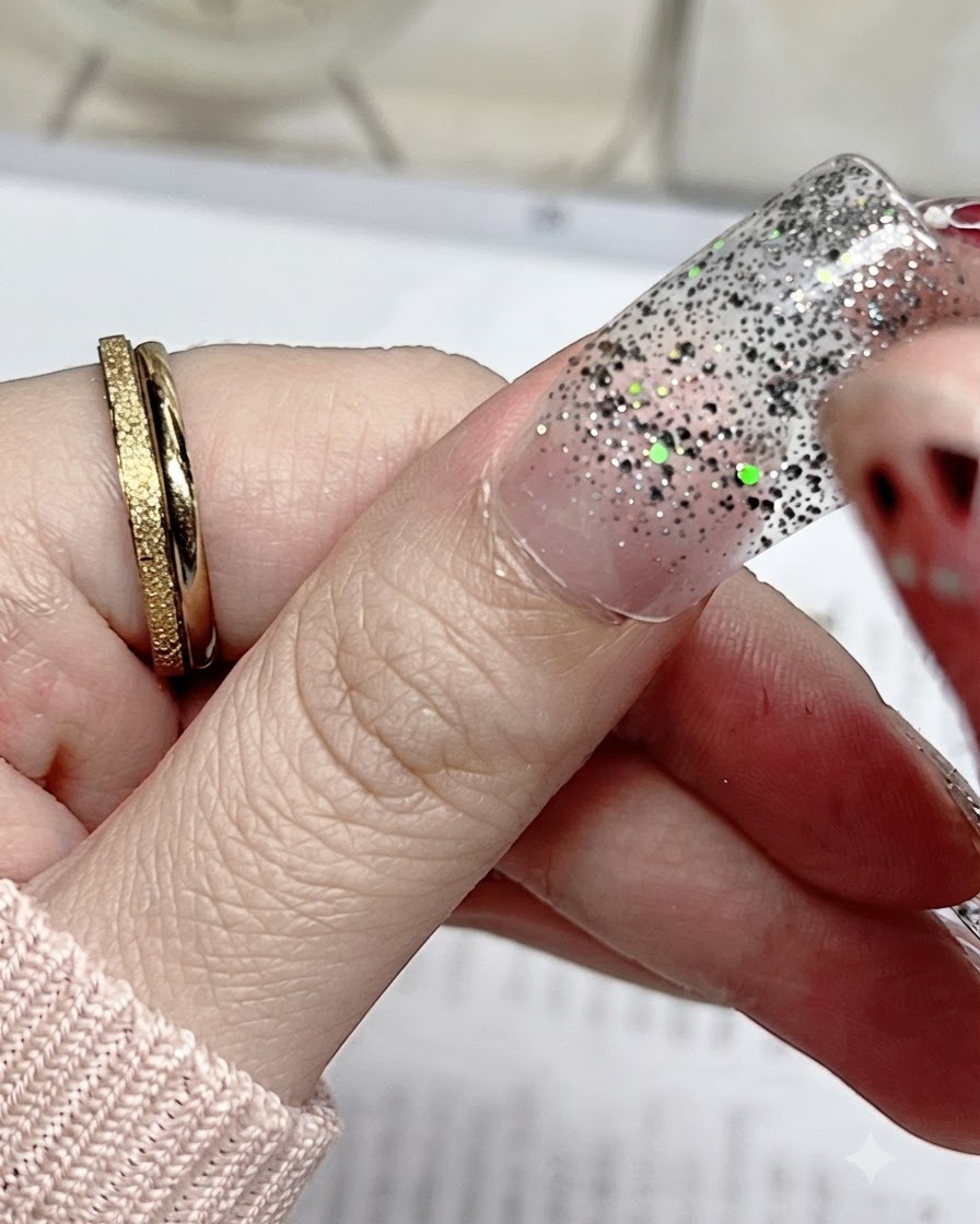 Primo piano di un adesivo per unghie glitterato argento allineato con precisione alla cuticola di un pollice naturale.