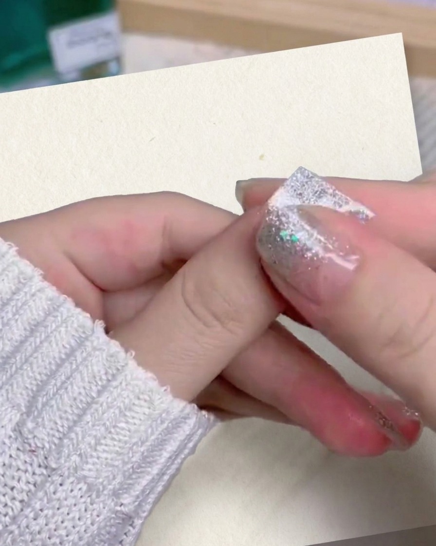 Un primo piano del pollice e dellindice di una persona che premono e lisciano saldamente ununghia finta con gradiente glitter argento sul proprio dito.