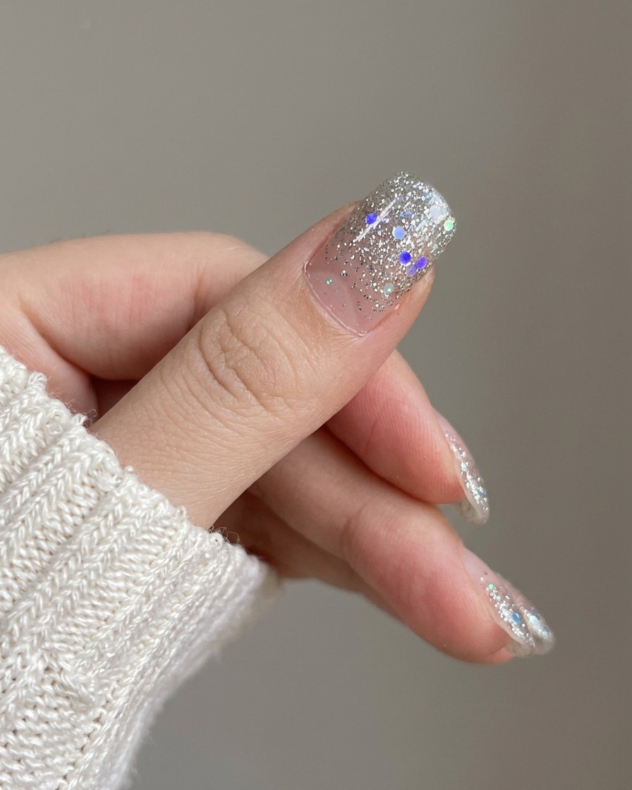 Un primo piano che mostra la nuova unghia con gradiente glitter argento applicata sullindice accanto a unghie non smaltate.