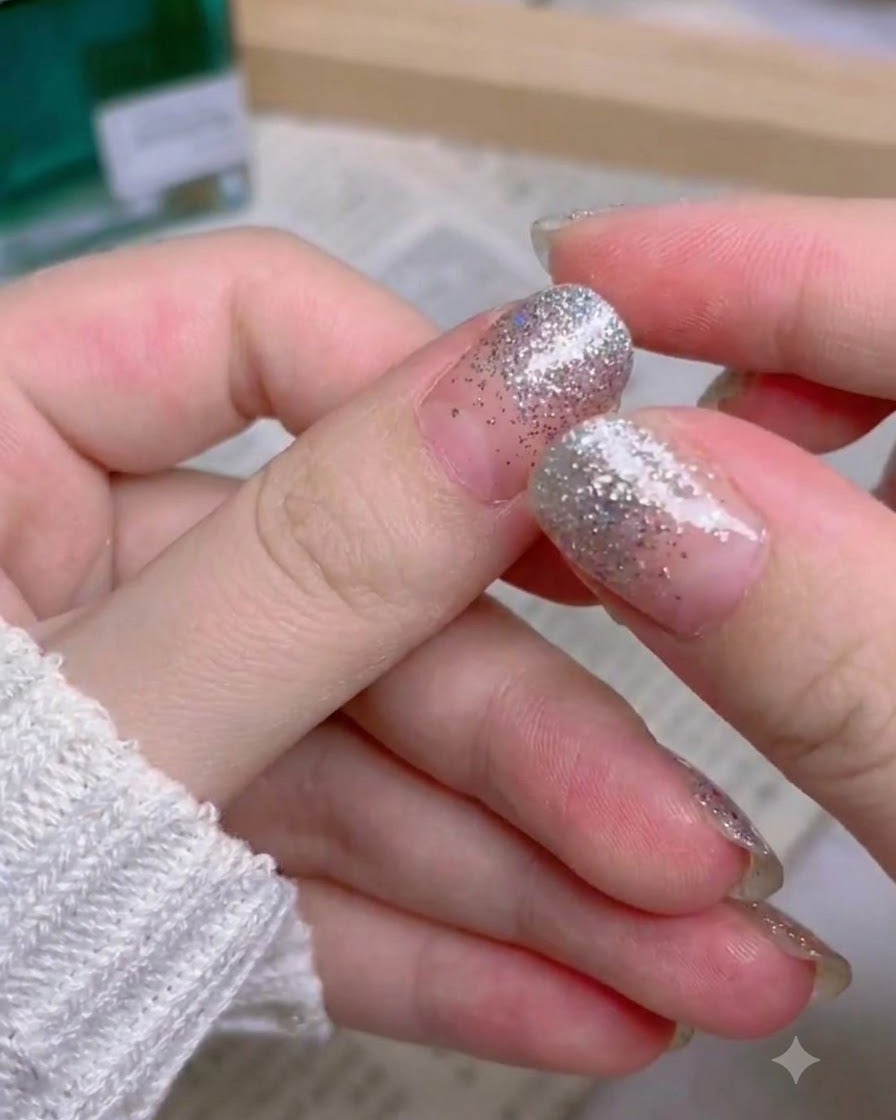 Una mano che mostra il set completo finito di unghie press-on con gradiente glitter argento.