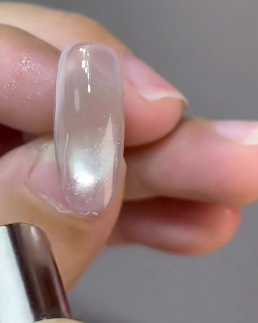 Un piccolo magnete circolare che modella un riflesso cat-eye a sfera di vetro riflettente su ununghia.