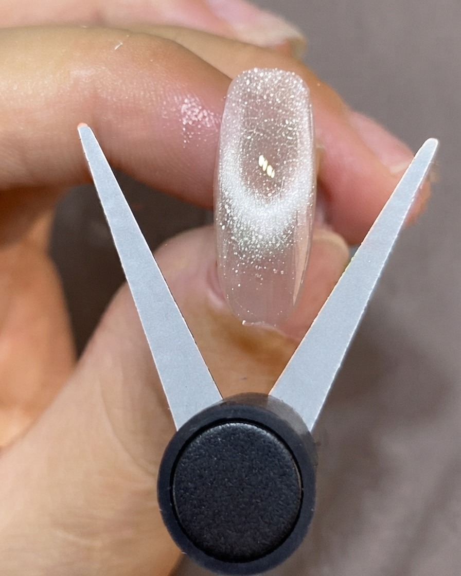 Uno strumento magnetico a forma di V tenuto sopra ununghia traslucida per creare una punta cat-eye francese brillante.