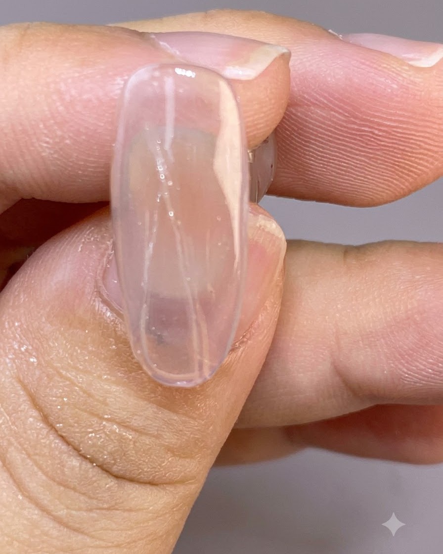 Un primo piano di ununghia trasparente che mostra linee sottili e delicate di piuma dipinte sulla superficie bagnata.