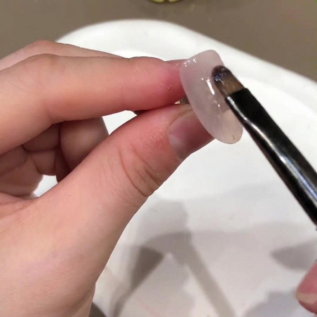Un pennello da unghie applica un colore di base in gel rosa nude sulla superficie di ununghia finta.