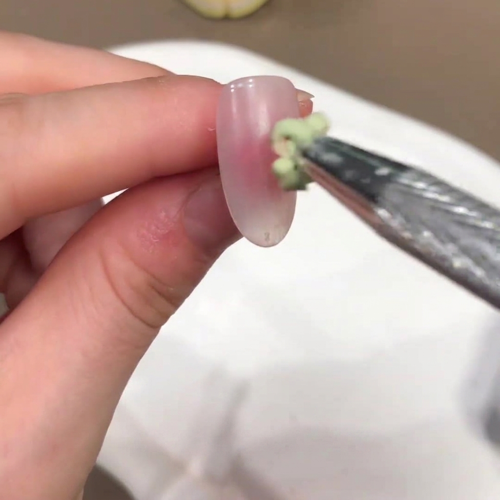 Un piccolo pennello applica una goccia di gel color verde al centro di ununghia rosa nude.
