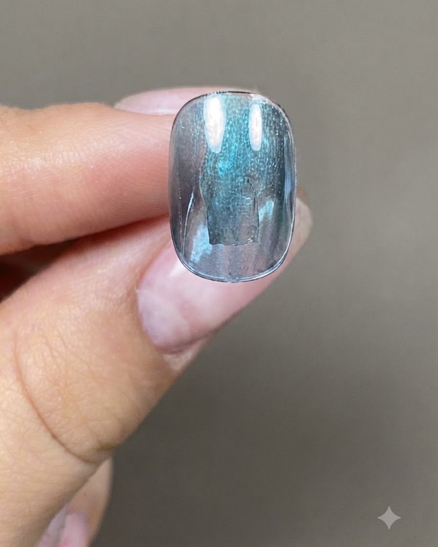 Un pennello da unghie che applica uno spesso strato di gel cat eye blu-verde su ununghia artificiale.