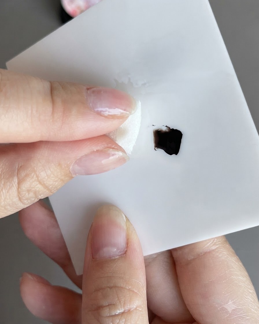 Una spugna che raccoglie lo smalto gel nero e lo tampona su un blocchetto di carta bianca.