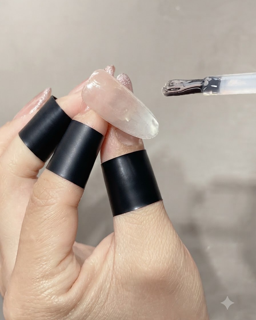 Un pennello per smalto che applica uno strato spesso di top coat lucido trasparente su ununghia cat-eye con perla di vetro finita.