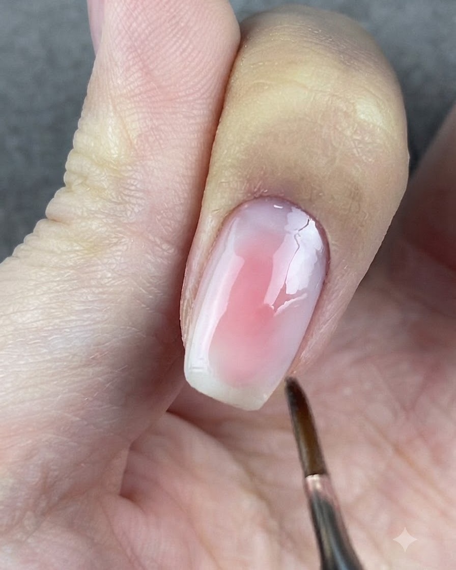 Un pennello a testa tonda tampona delicatamente i bordi del gel rosa su ununghia.