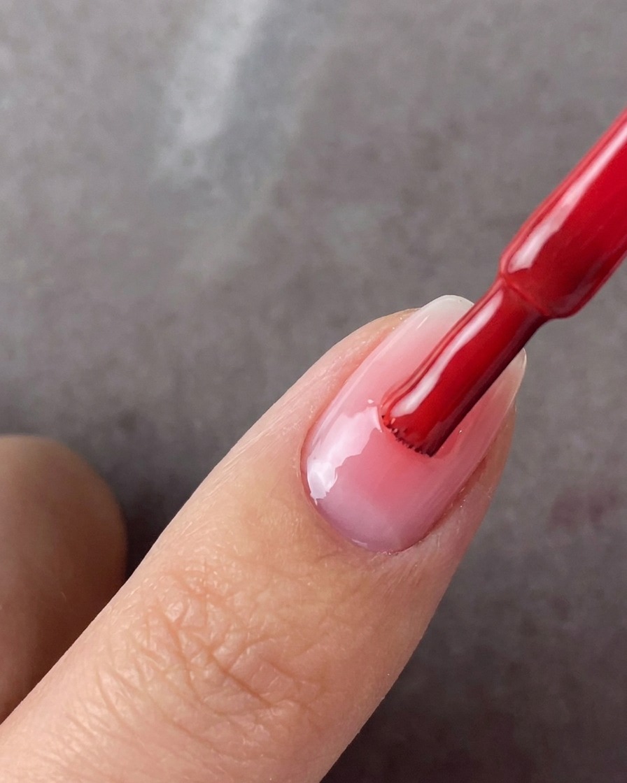 Un pennello per smalto rosso applica una seconda mano di gel rosa al centro di ununghia curata.