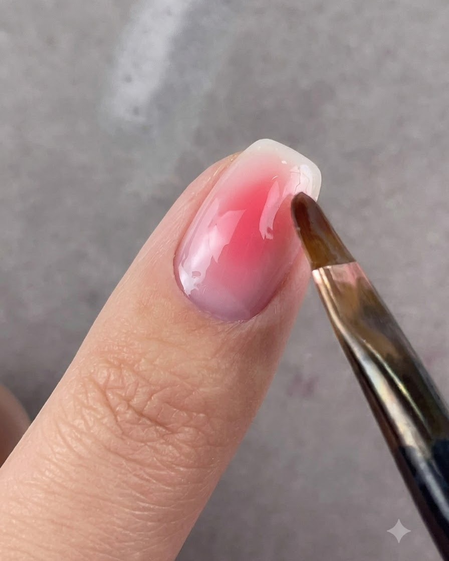 Un pennello a testa tonda sfuma delicatamente i bordi del gel rosa su ununghia.
