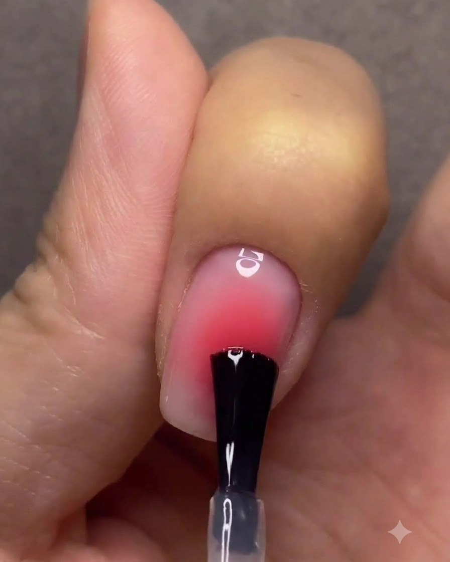 Una mano con unghie sfumate finite che polimerizzano sotto una lampada per unghie UV/LED rosa.