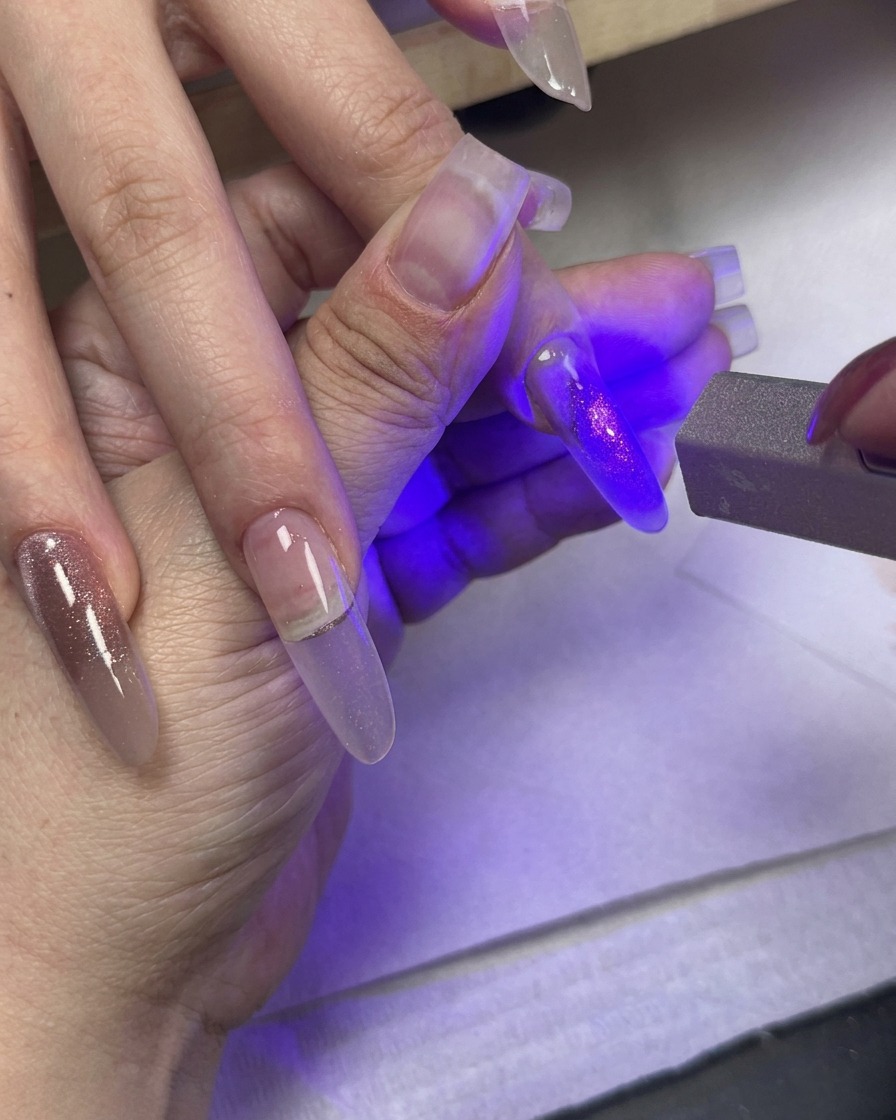 Una luce UV che catalizza ununghia dipinta mentre altre dita con gel cat-eye sfumato riposano nelle vicinanze.
