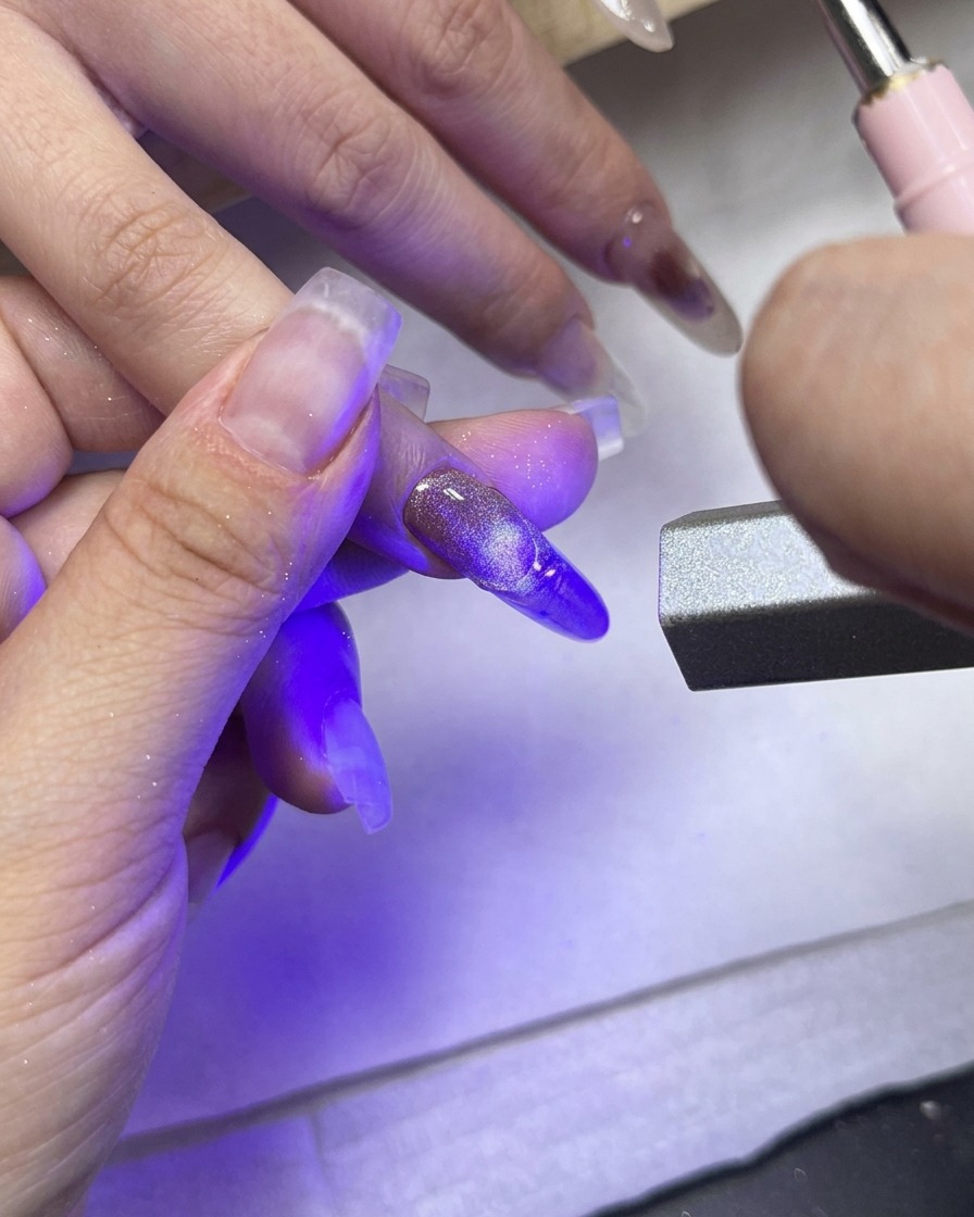 Una luce di polimerizzazione UV/LED puntata direttamente sul dito medio che mostra la French tip texturizzata.