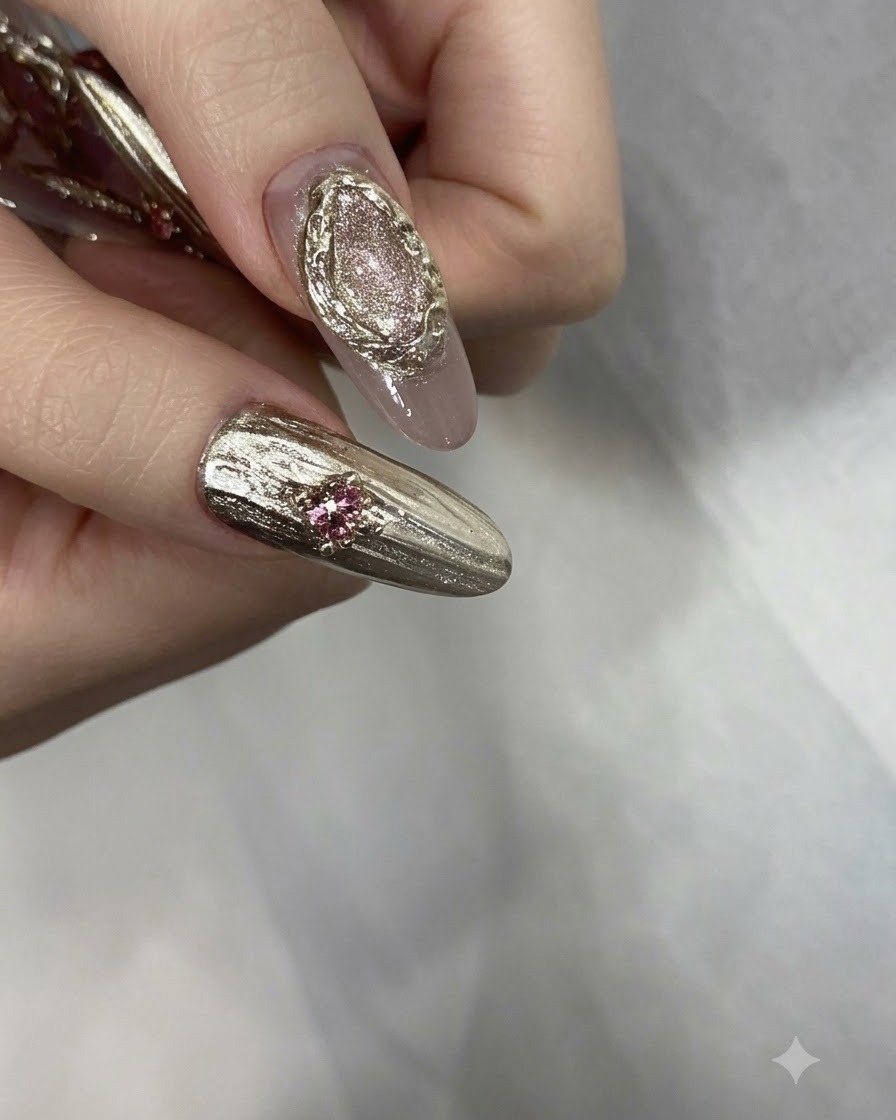 Dita con manicure finita decorate con strass rosa, perline dorate e dettagli cromati texturizzati.