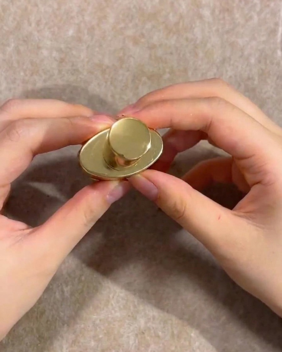 Mani che reggono il tappo dorato di un flacone di gel semipermanente nude.