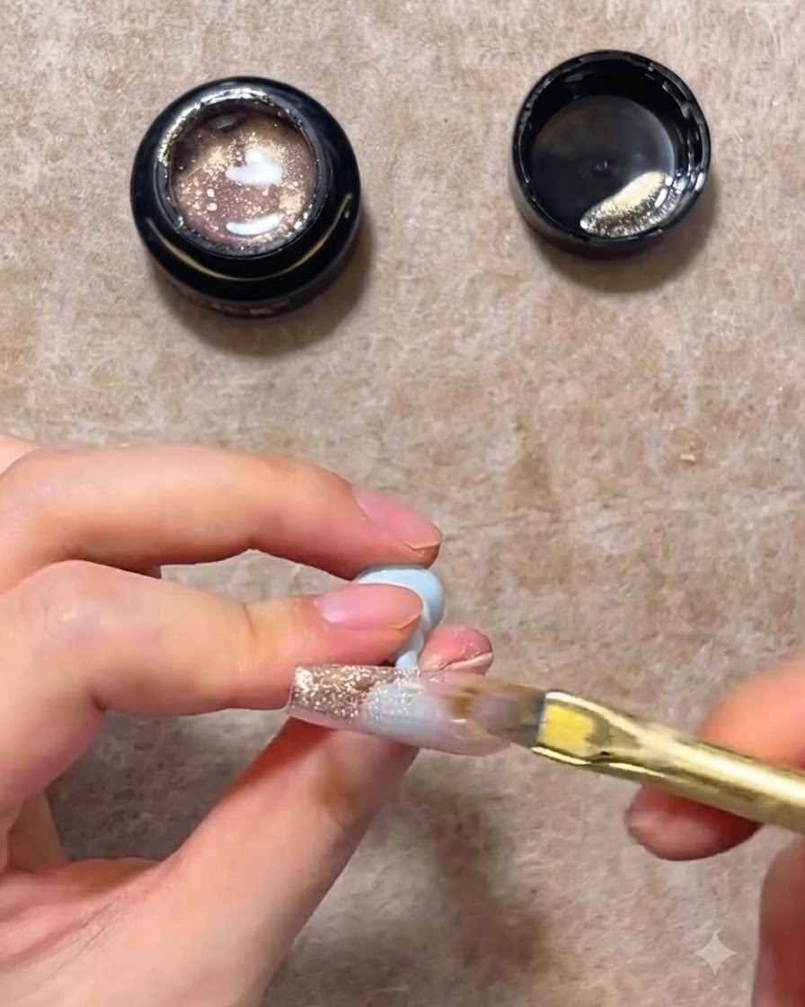 Un pennello piatto per unghie che spinge il gel cat eye rosa oro verso il basso su una tip trasparente per creare una sfumatura.