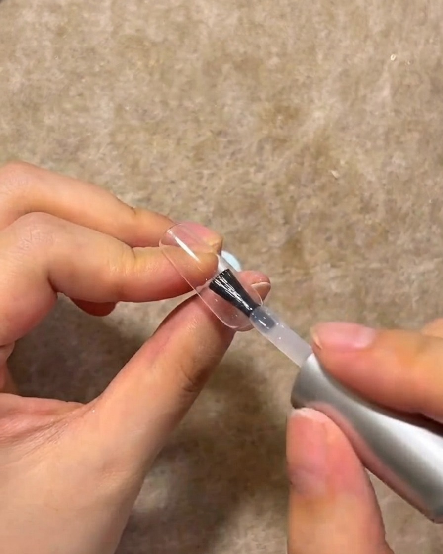 Un pennello per unghie che applica uno strato di gel costruttore trasparente sulla superficie di ununghia decorata.