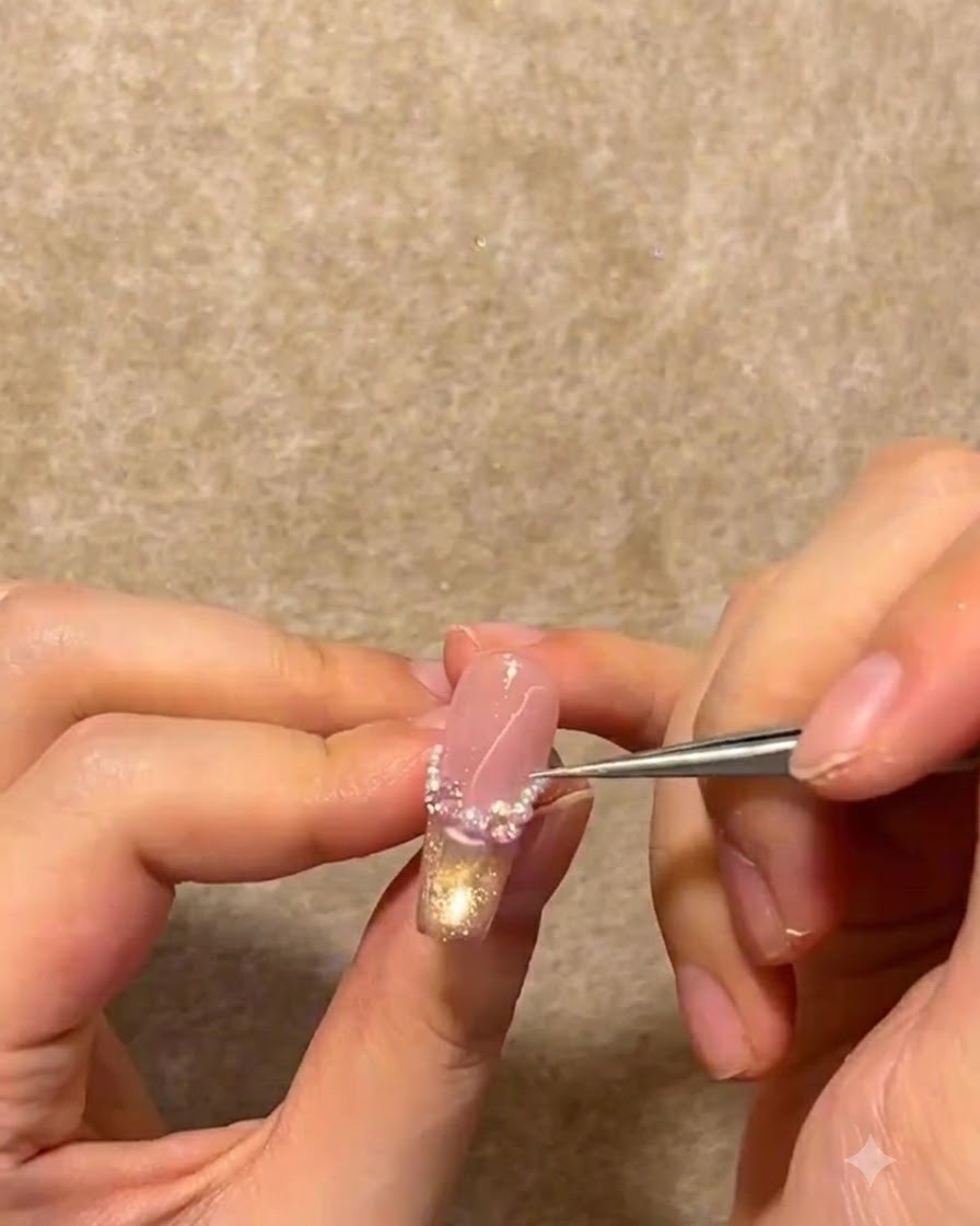 Un paio di pinzette metalliche che posizionano minuscole perle bianche e strass lungo la linea del sorriso French di ununghia.