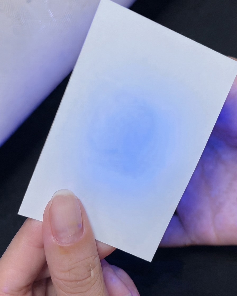 Una mano che tiene una carta bianca che mostra un test di riflessione della luce UV blu sottostante.