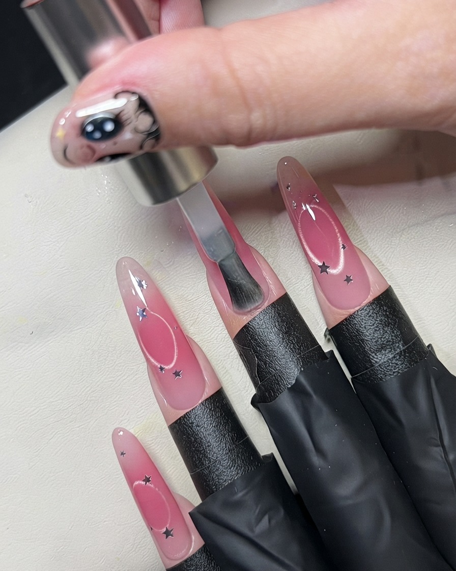 Un pennello che applica uno strato trasparente su ununghia decorata con paillettes a stella.