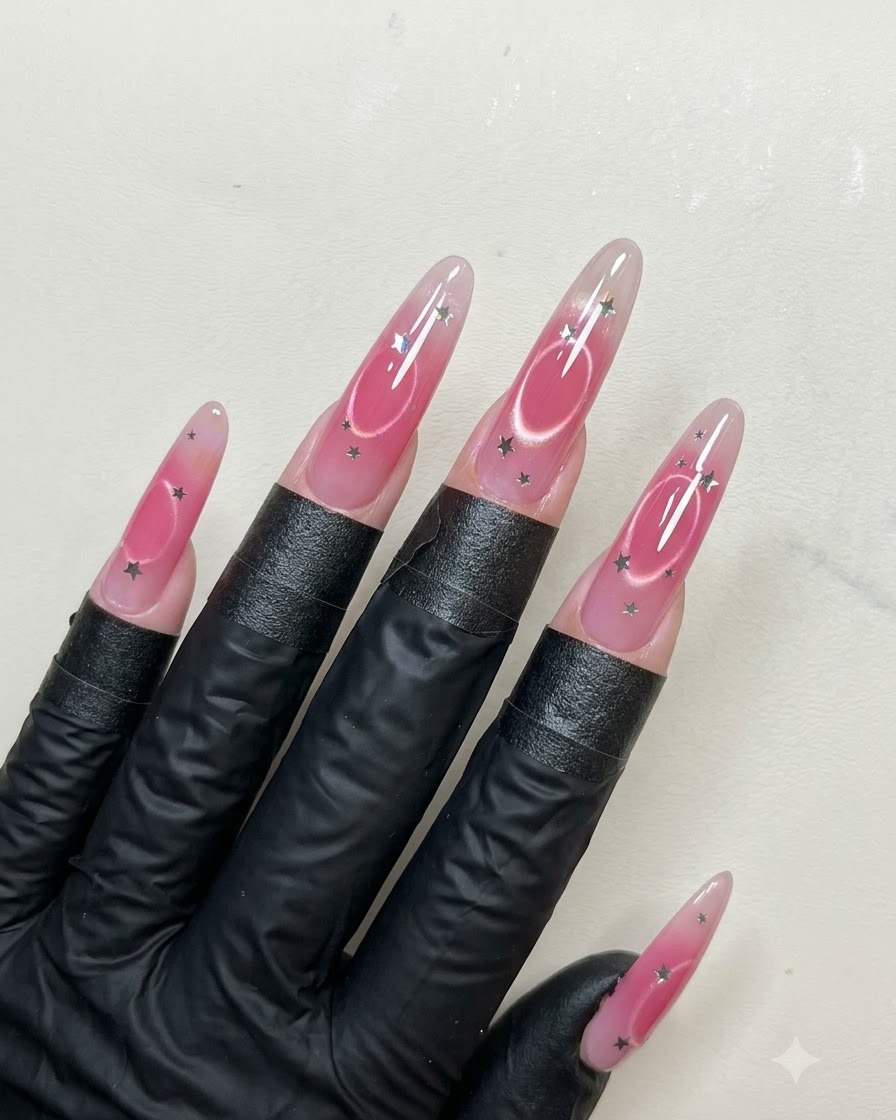 Un pennello per unghie che applica un denso strato di top coat lucido su unghie lunghe a mandorla decorate con paillettes a stella e nail art cat eye.